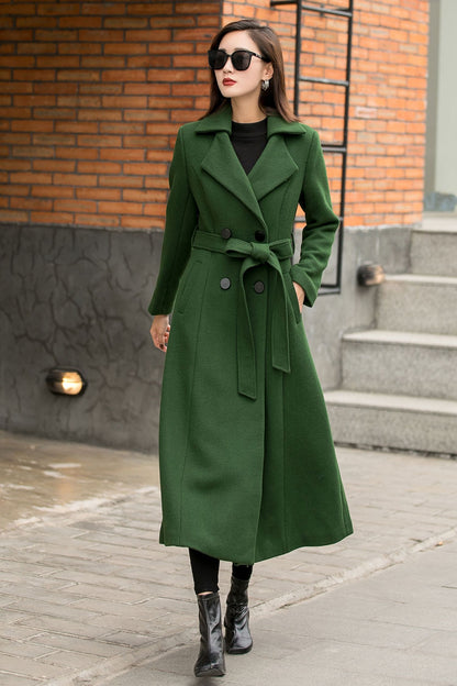 A woman wearing a green, vintage-style maxi wool coat with a double-breasted button closure and two side seam pockets, paired with black sunglasses and black boots.