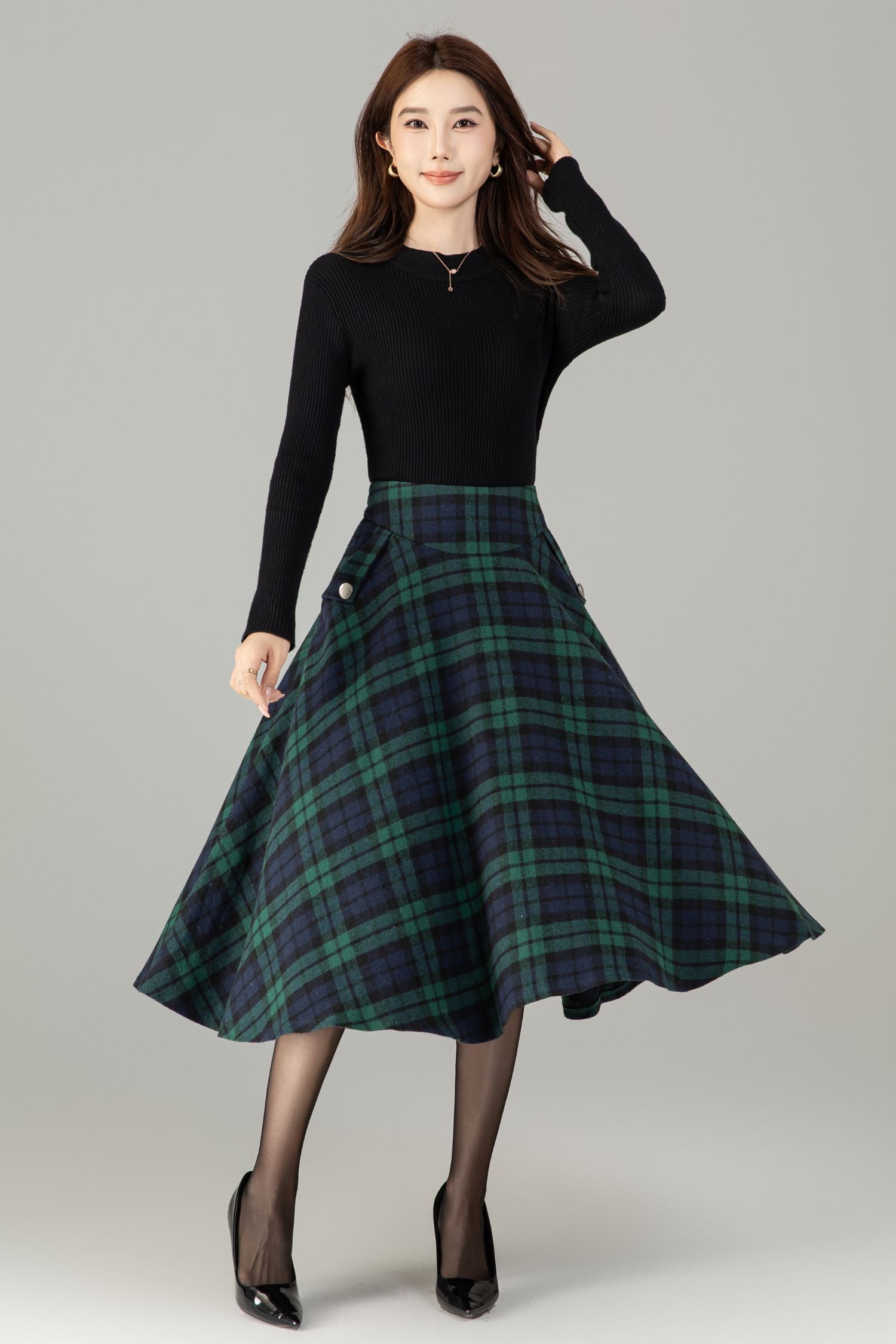 Woman wearing a black top and plaid skirt on a gray background