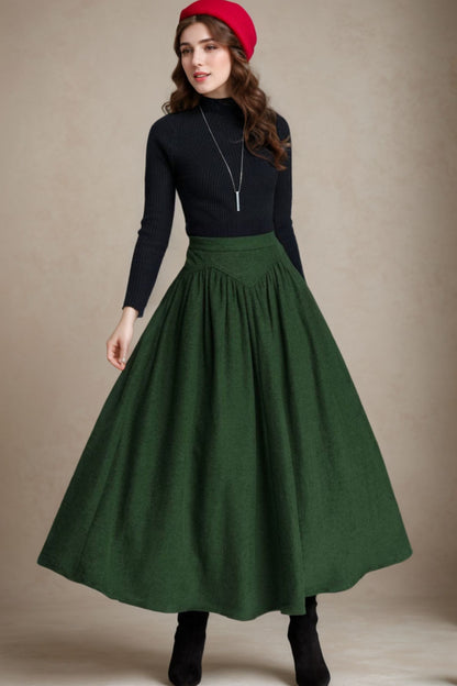 A woman wearing a vintage inspired maxi skirt in green, with a pleated detail and a unique waist design. She is also wearing a black top and a red hat.