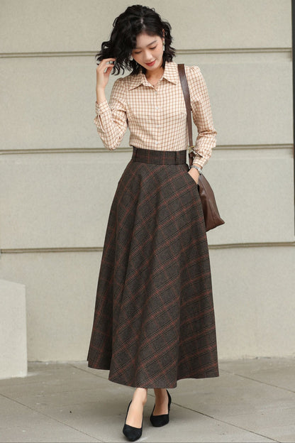 Woman wearing a checkered shirt and plaid skirt standing against a light-colored wall.