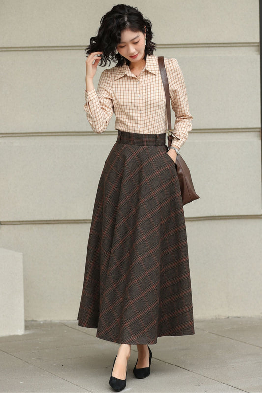 Woman wearing a checkered shirt and plaid skirt standing against a light-colored wall.
