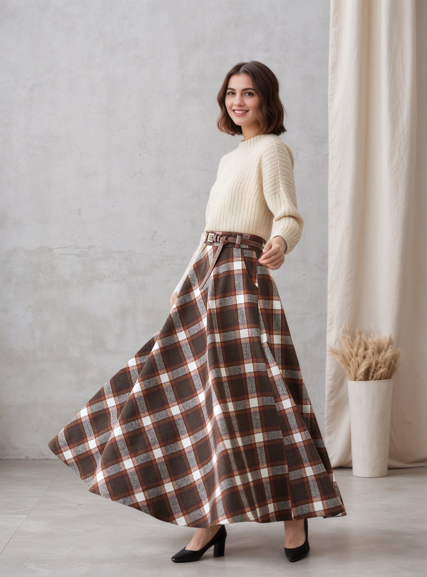 Woman wearing a white sweater and brown plaid skirt standing against a gray wall.