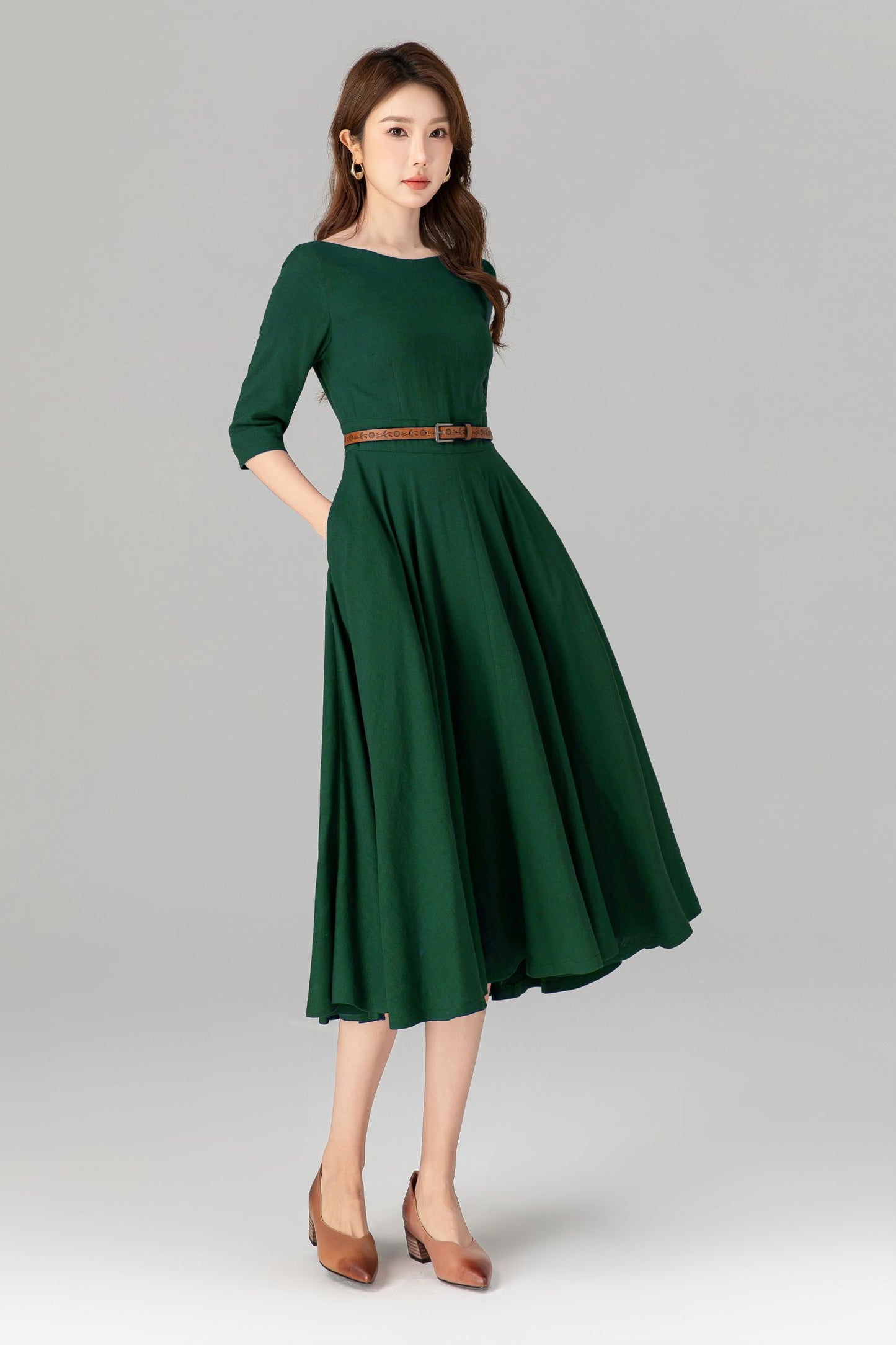 Woman wearing a green dress with a brown belt on a gray background