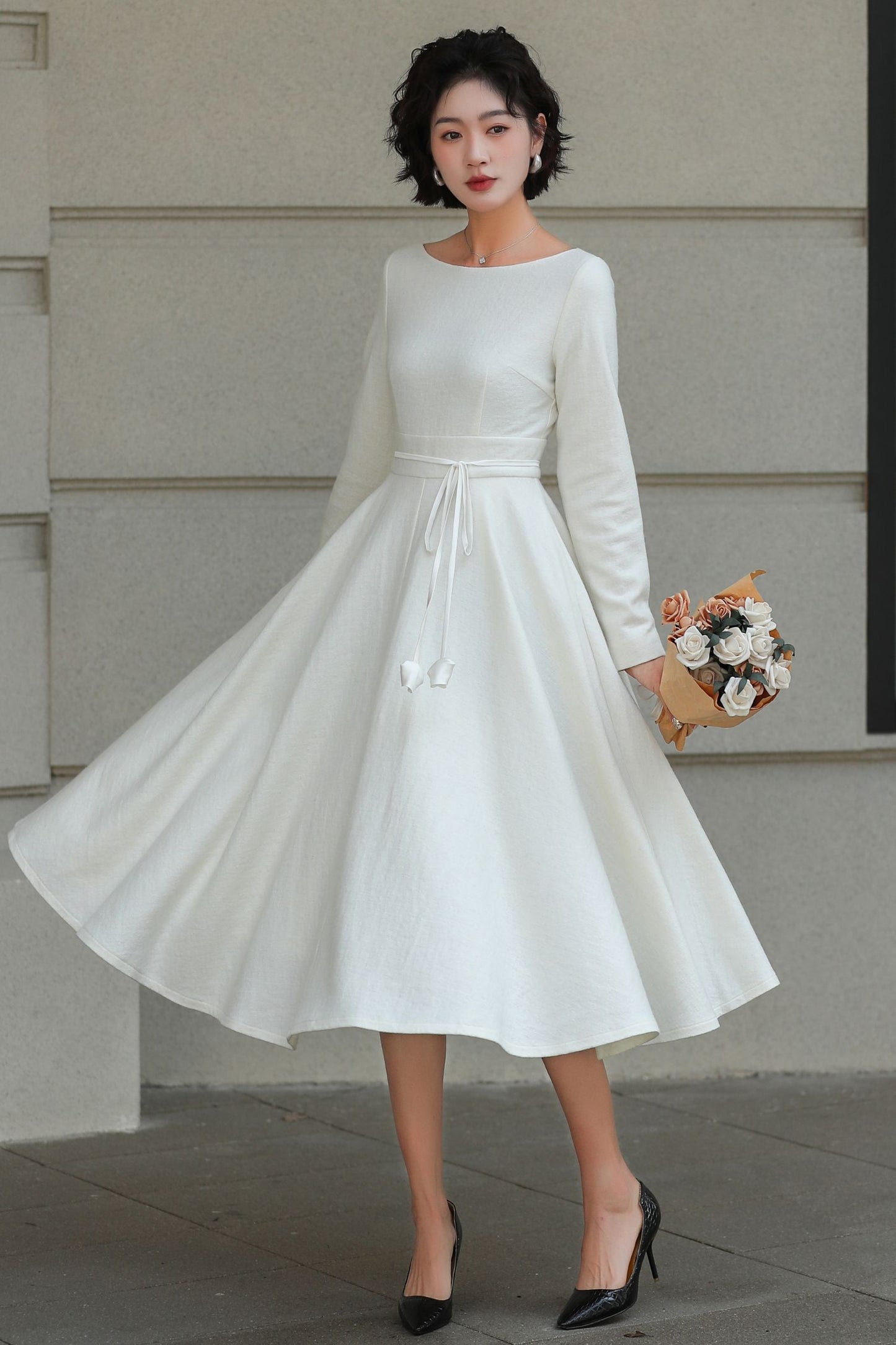 Woman wearing a white dress holding flowers against a plain background