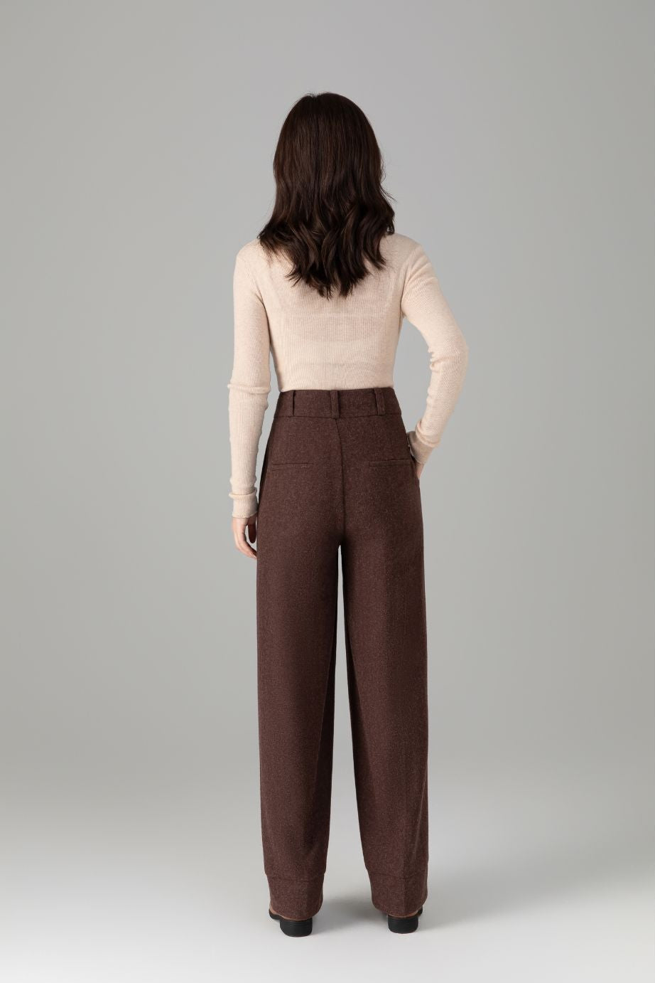 Woman wearing brown high-waisted pants on a gray background