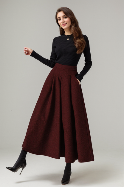 A woman wearing a gray A-line maxi wool skirt with a black long-sleeve top, standing with one hand in a pocket and the other by her side.