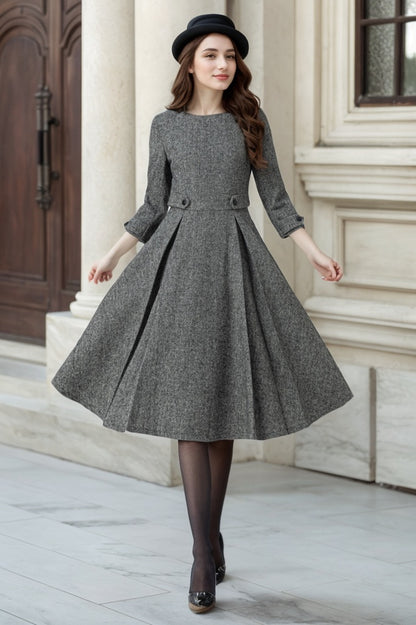 A woman wearing a gray wool fit and flare midi dress with a round neckline and three-quarter length sleeves. She is paired with black tights and heels.