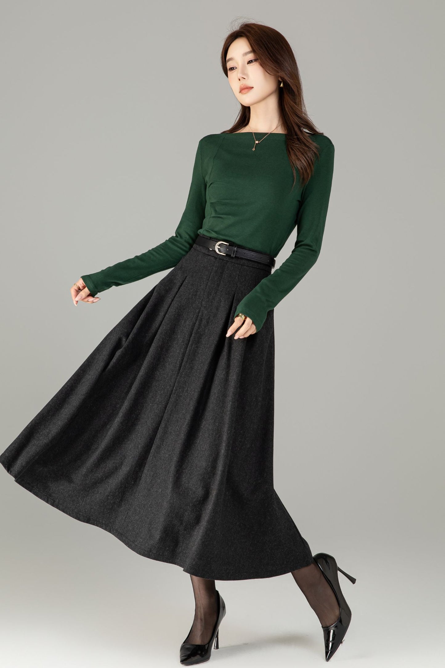 Woman wearing a green long-sleeve top and black skirt on a gray background