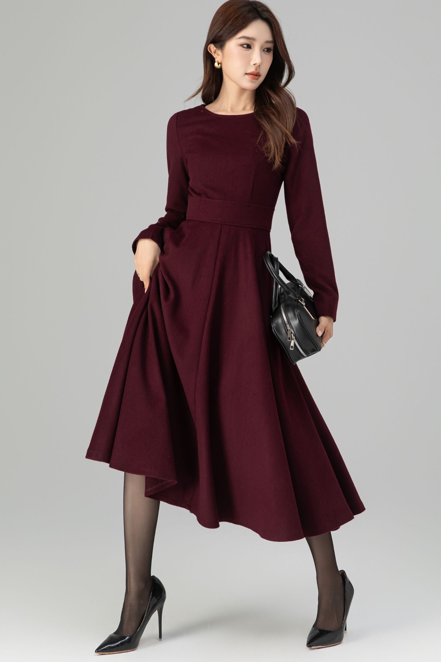 Woman wearing a burgundy dress with long sleeves on a gray background