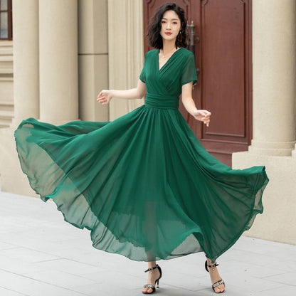 A woman wearing a deep green chiffon V-neck maxi dress with short sleeves and an ankle-length silhouette, standing in front of a building.