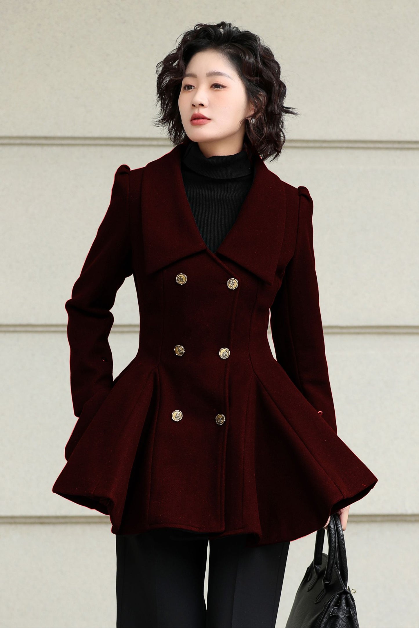 Woman wearing a dark red peacoat with gold buttons against a light background