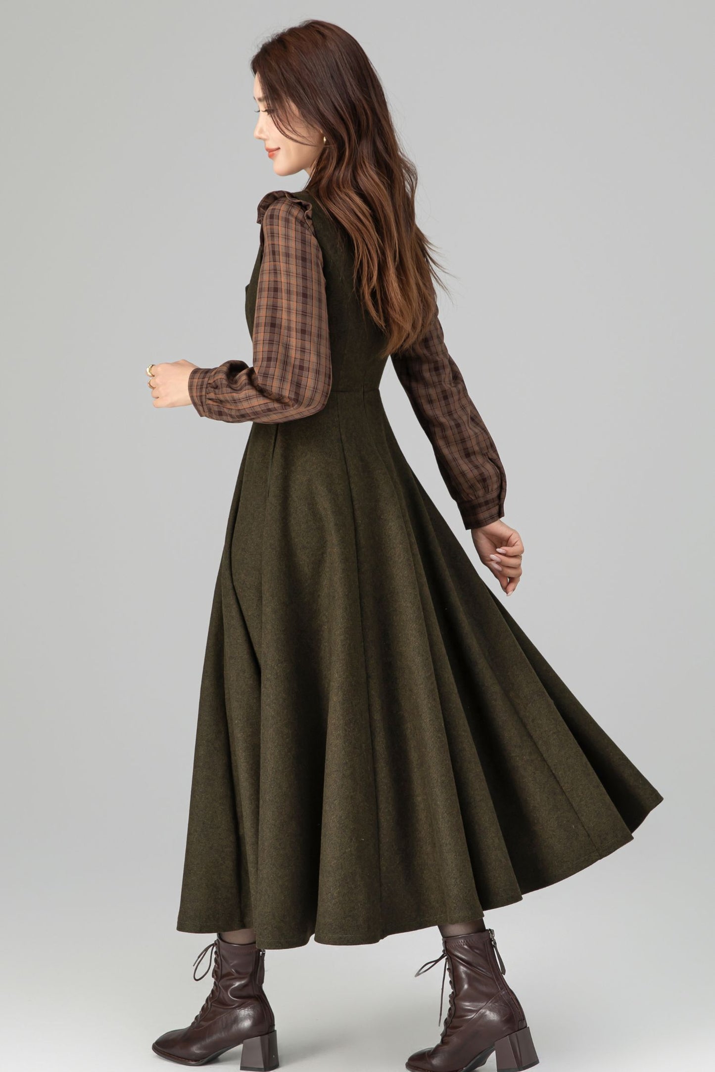 Woman wearing a long green dress with plaid sleeves on a gray background