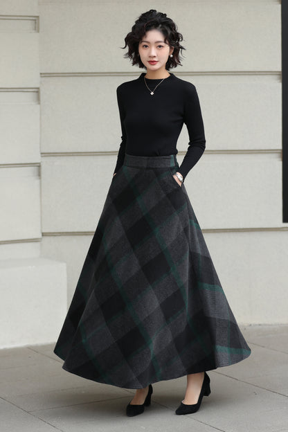 Woman wearing a black top and plaid skirt standing against a light-colored wall.
