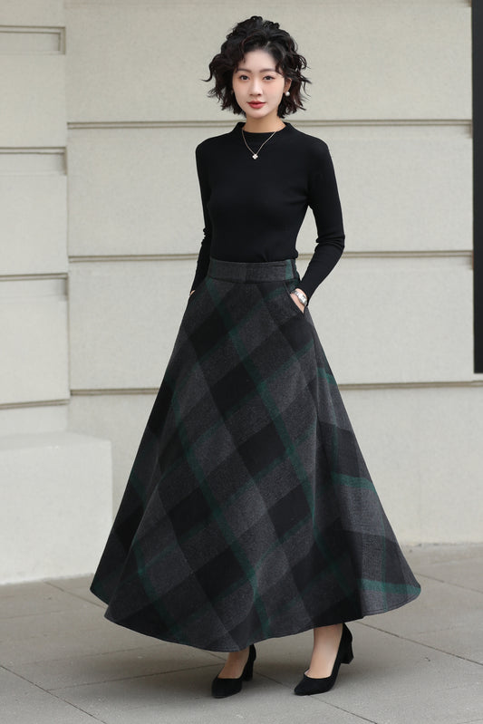 Woman wearing a black top and plaid skirt standing against a light-colored wall.