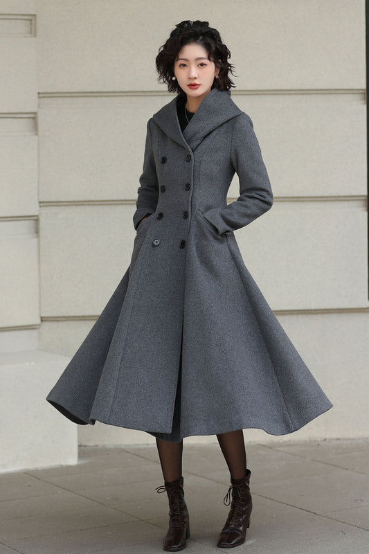 Woman wearing a long gray coat standing against a light-colored wall.