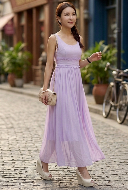 Woman in a lavender dress standing on a cobblestone street with buildings and plants in the background.