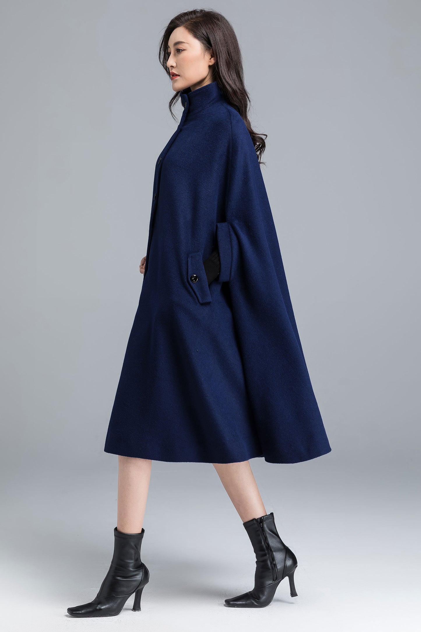 Woman wearing a long navy coat on a plain background
