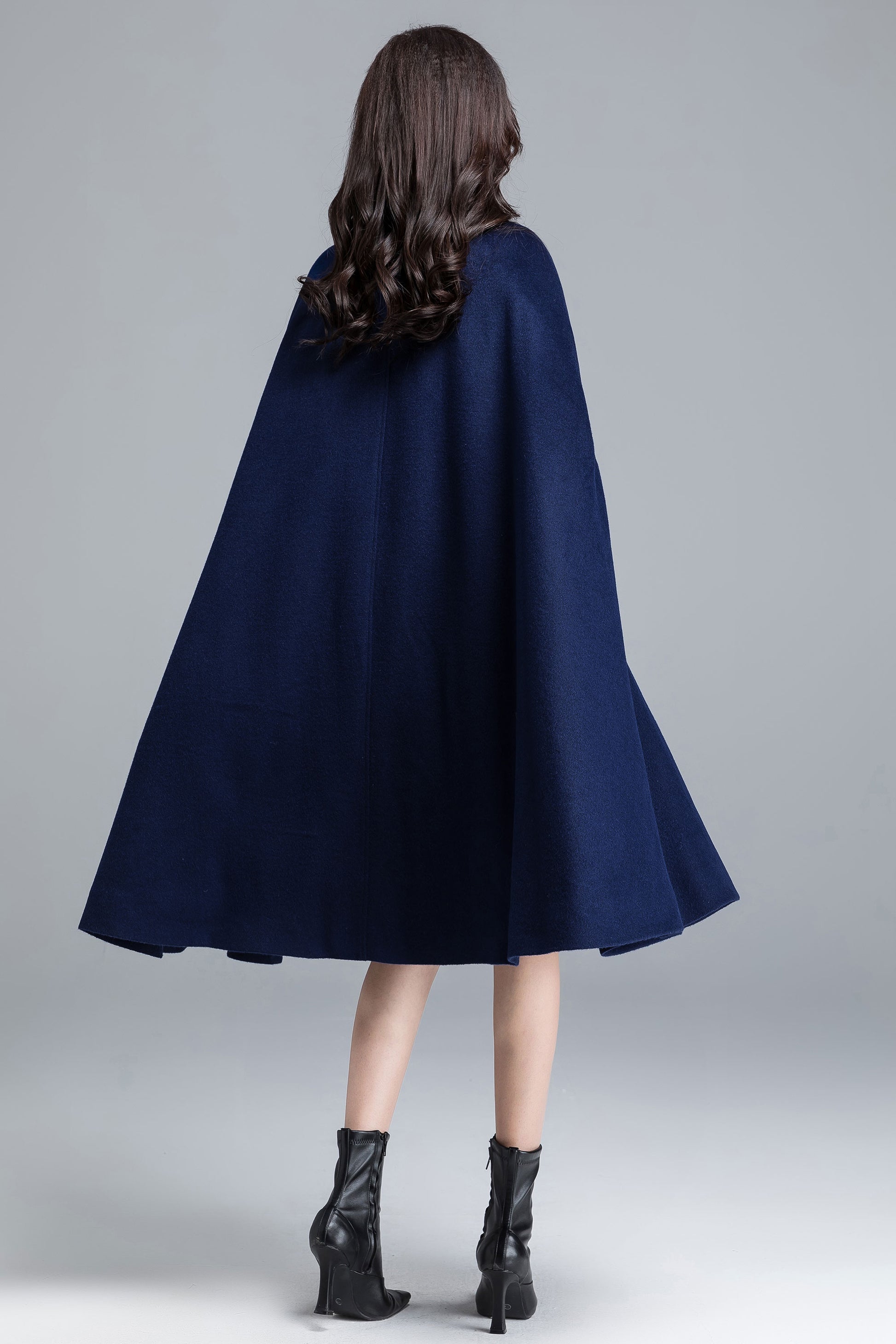 Woman wearing a navy blue cape against a gray background