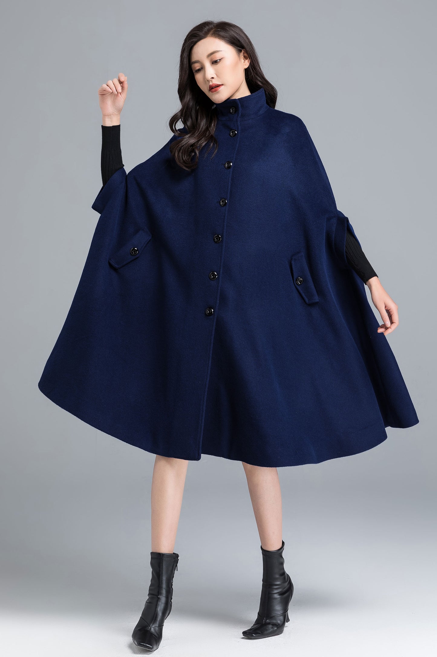 Woman wearing a navy blue cape over a black outfit on a gray background