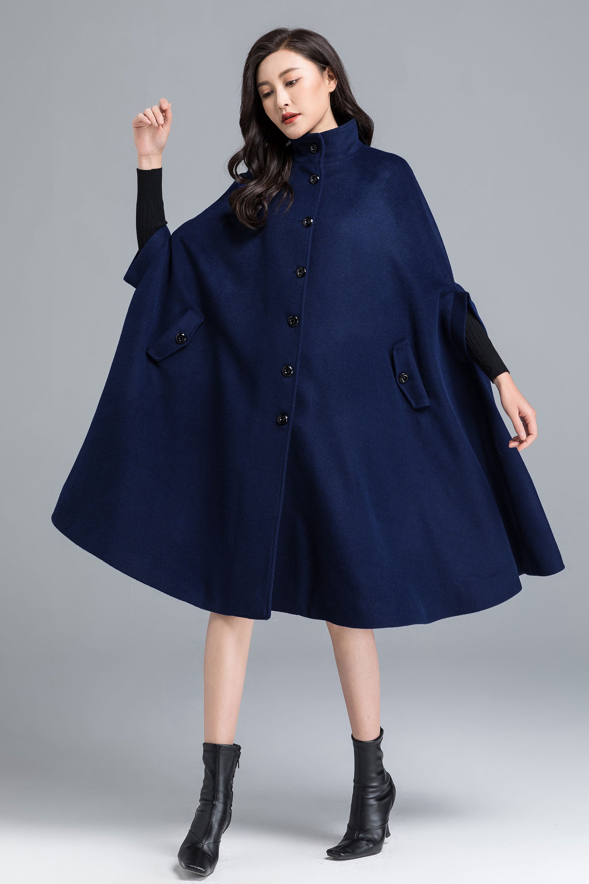 Woman wearing a navy blue cape over a black outfit on a gray background