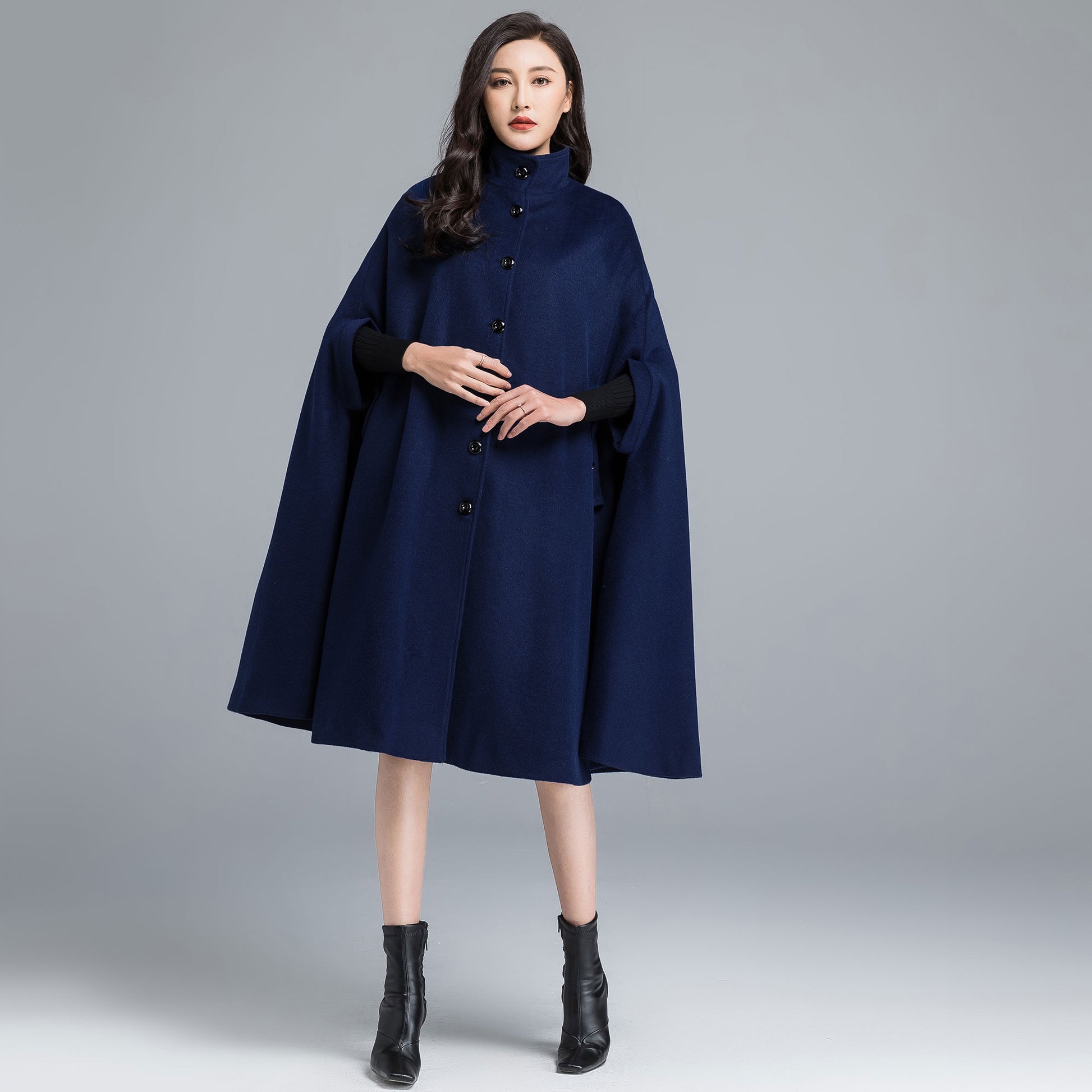 Woman wearing a navy blue cape over a black dress on a gray background