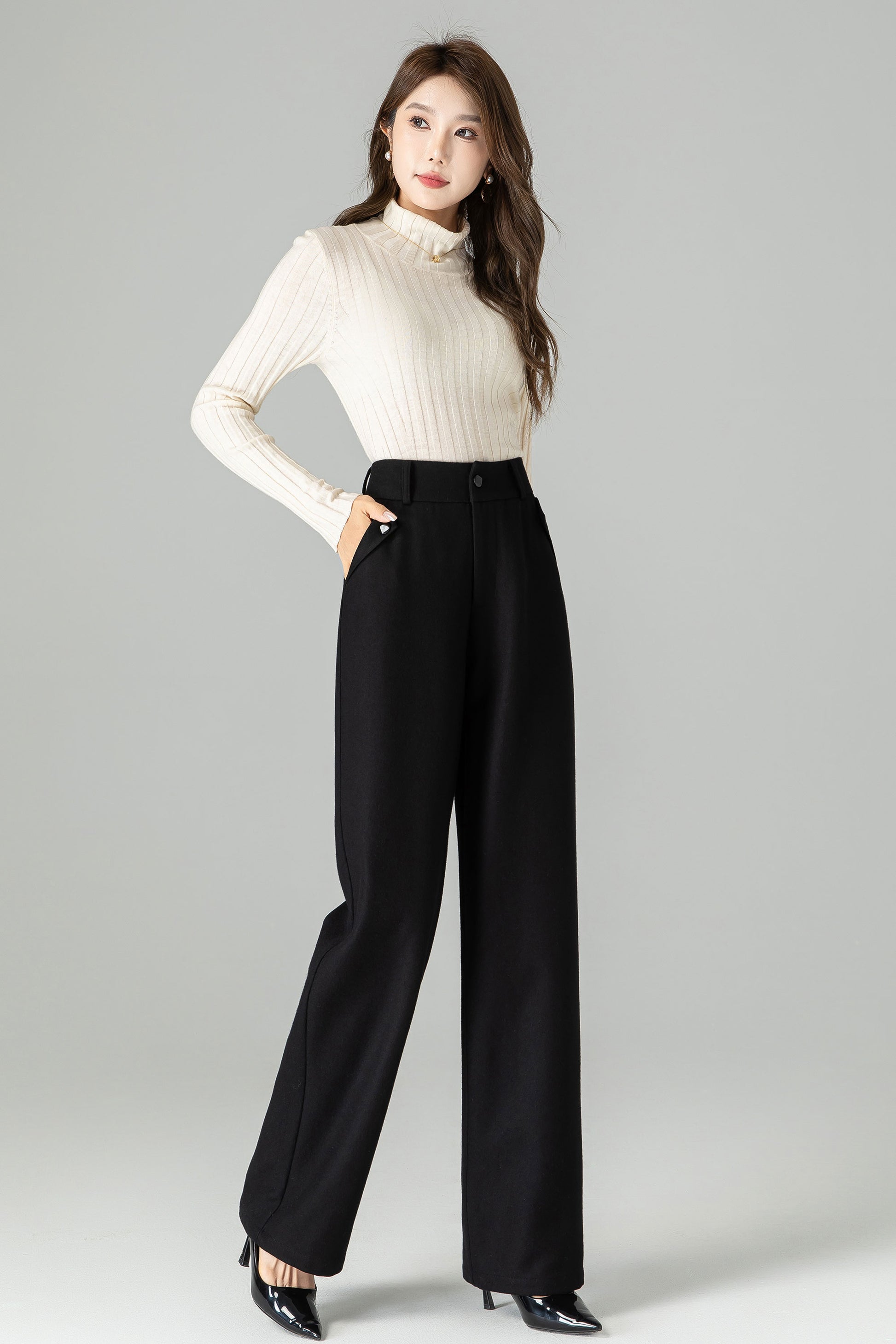 Woman wearing a white turtleneck and black high-waisted pants on a gray background
