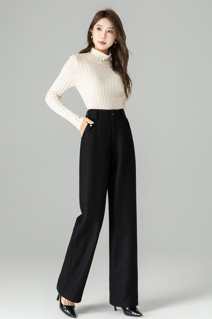 Woman wearing a white turtleneck and black high-waisted pants on a gray background