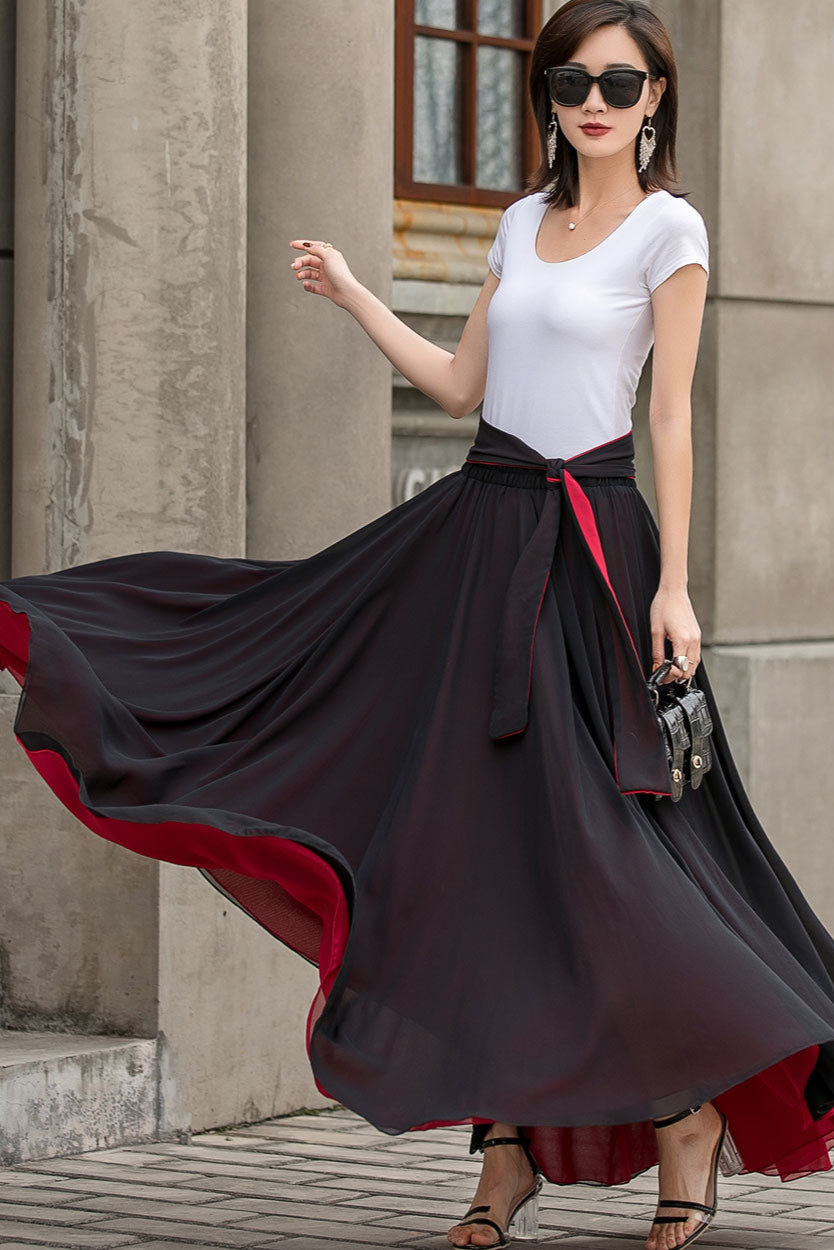 A woman wearing a black and red chiffon maxi skirt with a white t-shirt, featuring a striking contrast hem and an adjustable waist tie, standing outdoors.
