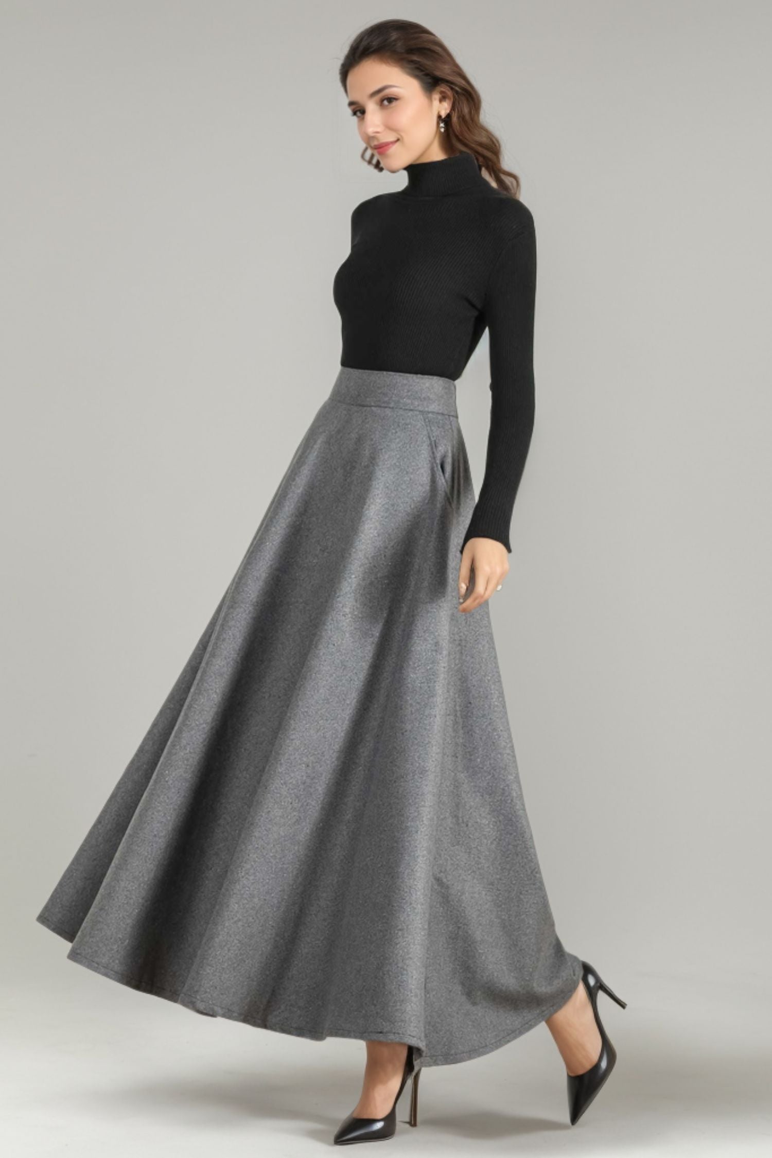 A woman modeling a vintage-style wool skirt with an elastic waist, in a gray color. The skirt reaches the ankle and has a satiny liner, featuring two side pockets and a right zip closure.