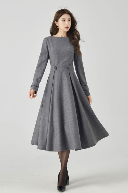 A woman modeling a gray fit and flare midi wool dress with round neckline and long sleeves. The dress is midi calf length and features a back zipper closure.