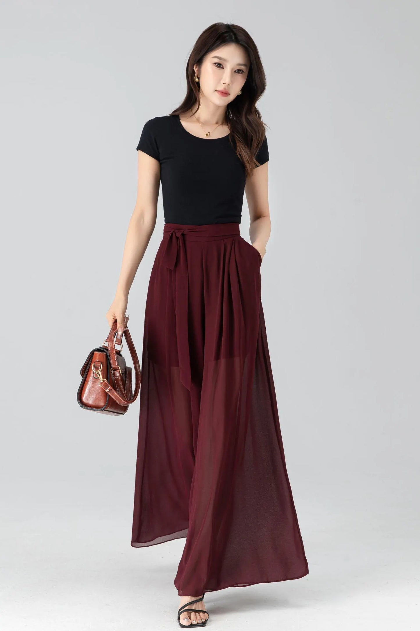 May include: A black short-sleeve top paired with a burgundy wide-leg skirt. The skirt features a high waist with a tie and pockets. A brown leather handbag with a shoulder strap is also visible.