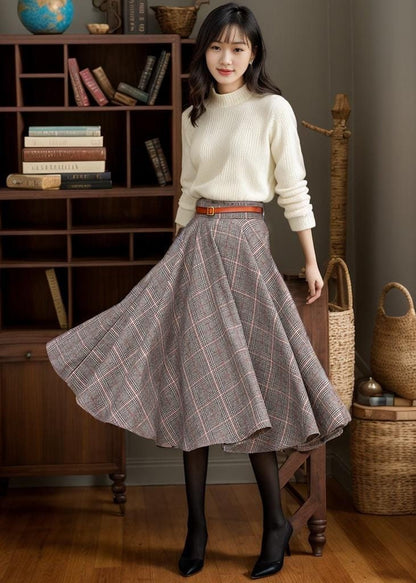 May include: A gray and pink plaid midi skirt with a high waist and A-line silhouette. The skirt is made of a wool-blend fabric and features a brown leather belt.  It is paired with a cream-colored turtleneck sweater. The skirt has a vintage or retro styl