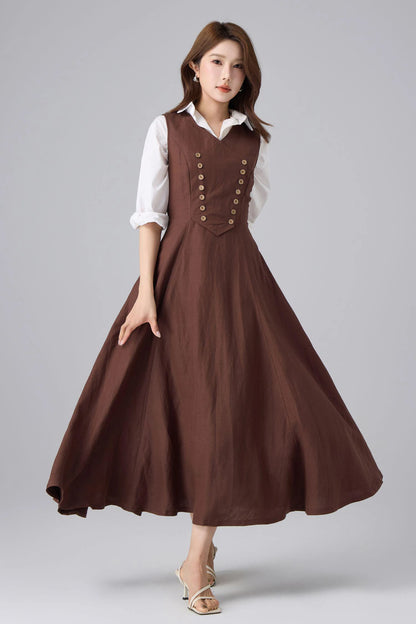 May include: A brown sleeveless dress with a white collared shirt underneath. The dress features a series of gold buttons down the front and a flared skirt. The model is wearing white sandals.