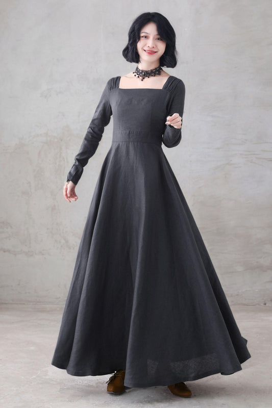 May include: A dark gray, long-sleeved dress with a square neckline and a full skirt. The dress has a fitted bodice and a flowing skirt. The model is wearing a black choker necklace. The dress is made of a soft, flowing fabric.