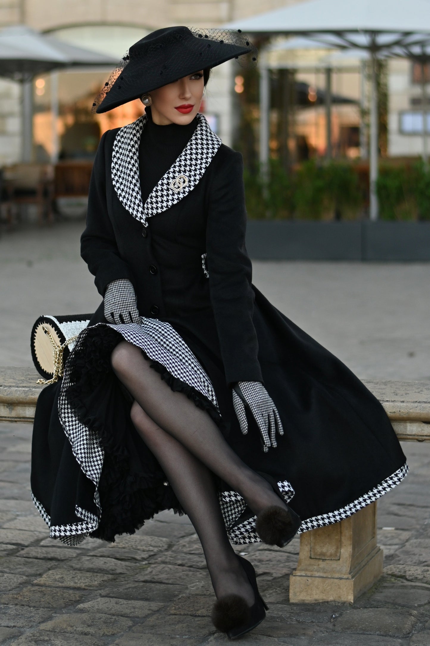 Woman in a black coat and hat sitting on a bench in an urban setting