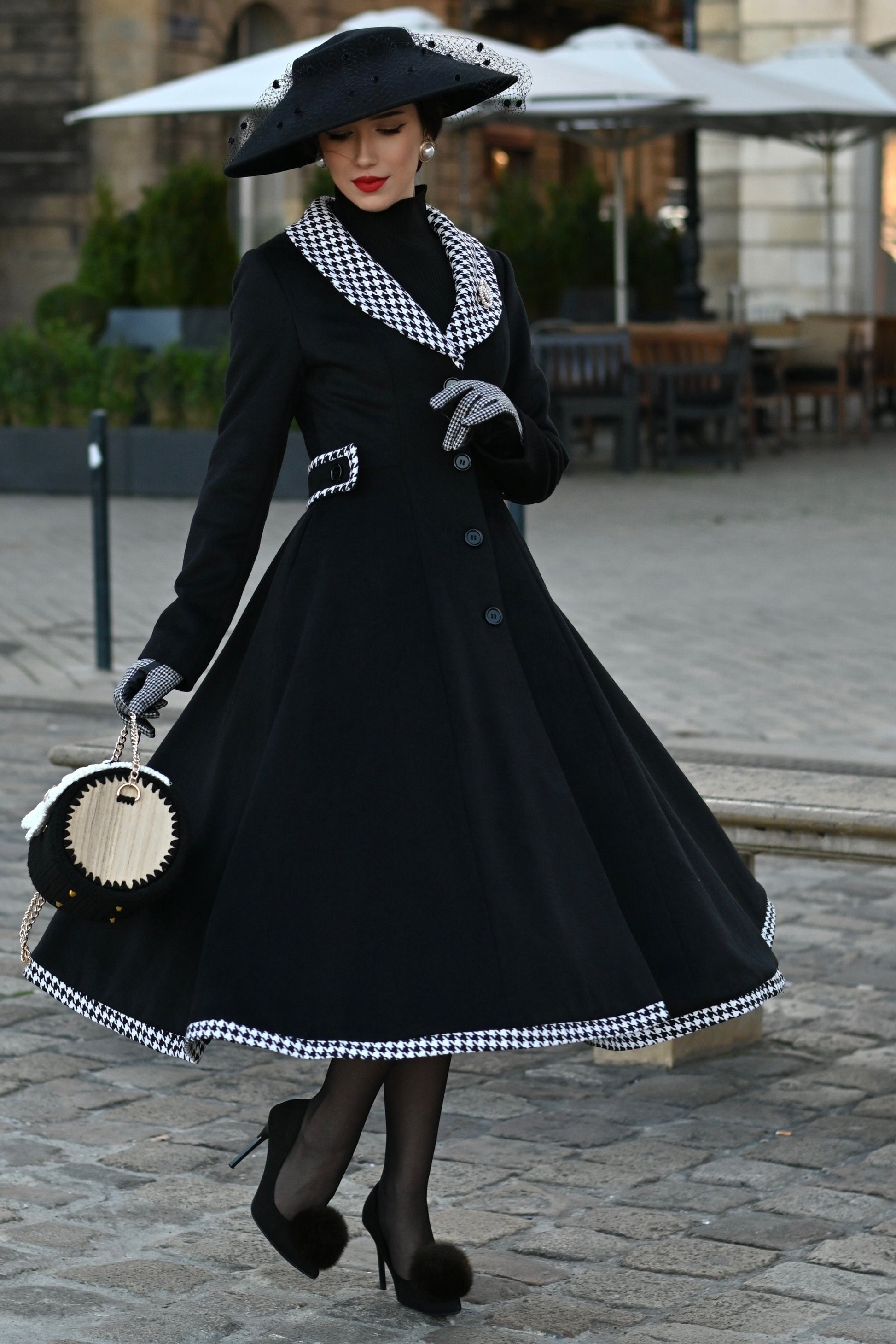 Woman in a black coat with white checkered details walking on a street.