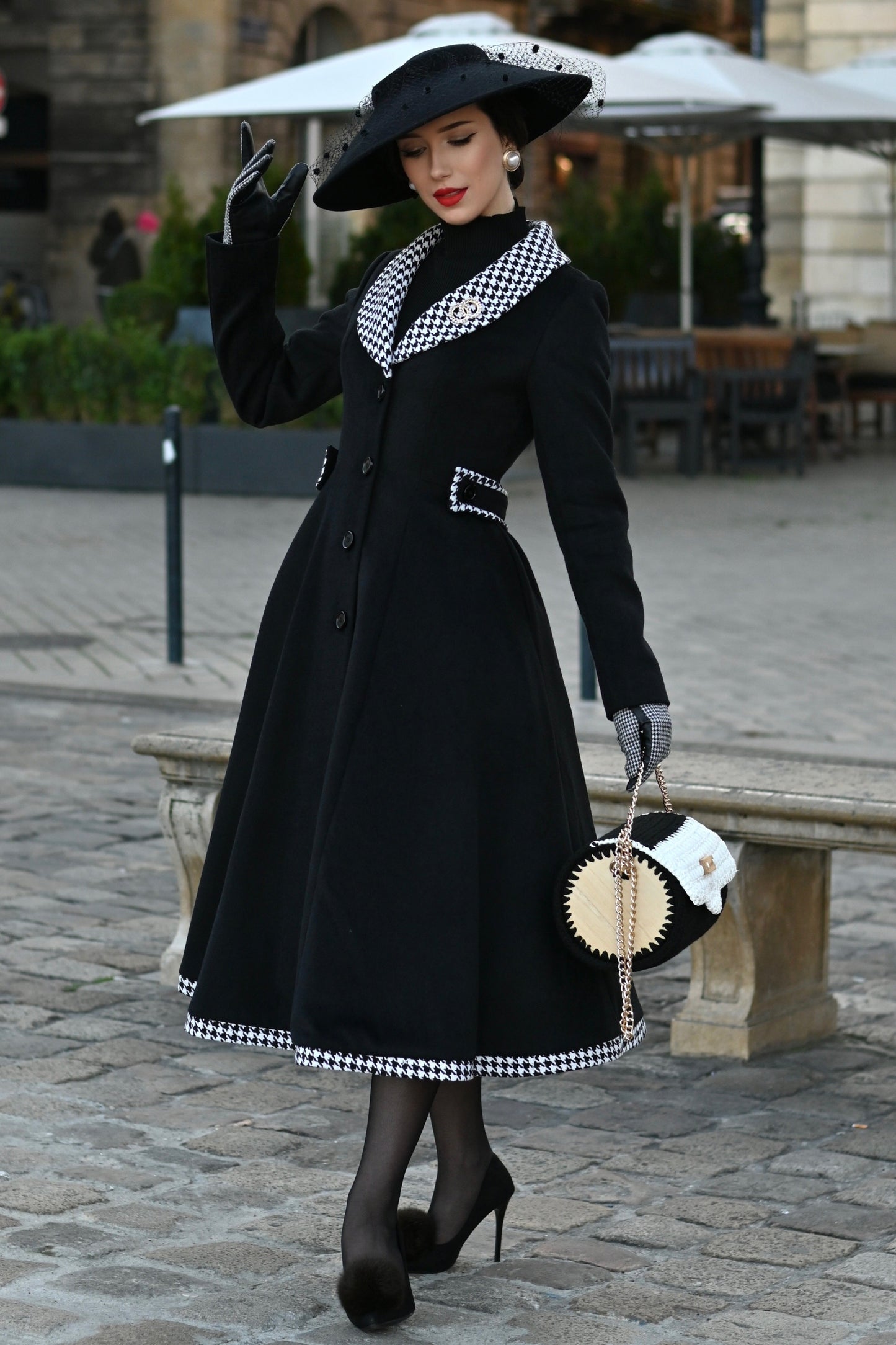 Woman in a black coat and hat walking on a city street.