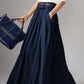 A navy blue linen maxi skirt with a high-waisted design, pleated waist, and side pockets. The skirt is ankle-length and the outfit is accessorized with a belt and handbag.