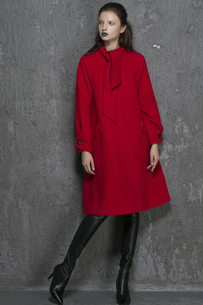 A woman modeling a red wool long sleeve coat with two big pockets. The model has a pale complexion and is wearing black boots.