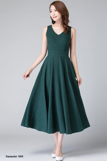 A woman wearing a green vintage inspired linen sleeveless swing party dress with round neckline and mid calf length.