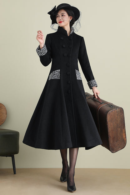 A woman in a black swing wool coat with two pockets and a decorative fabric belt, standing next to a suitcase.