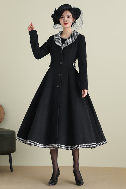 A woman modeling a long black wool coat with button closures, two side pockets, and a buttoned collar, paired with a black hat and black shoes.