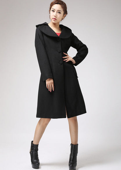 A woman modeling a long black wool coat with hip pockets and a round neckline.