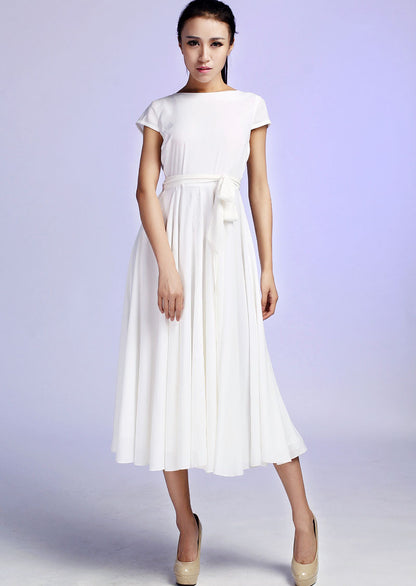 A woman wearing a white maxi chiffon dress with cap sleeves and a cinched waist, standing against a light background.