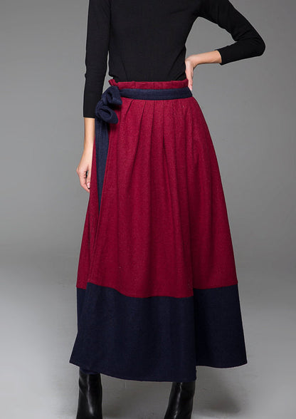 A wine red and blue maxi skirt with contrasting blue stitching and two large pockets on each side. It includes an adjustable belt with a bow at the front.