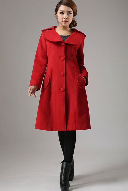 A woman standing wearing a red long sleeve winter cashmere coat with hip pockets and seam detailing.