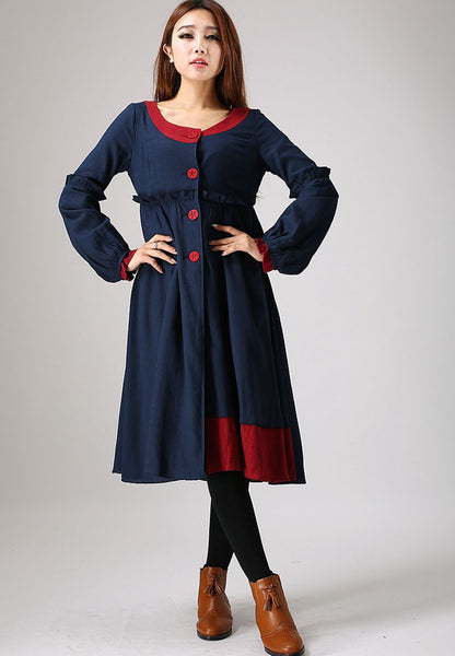 A woman standing and posing in a navy blue long shirt with red detailing on the collar and hem, paired with brown ankle boots.