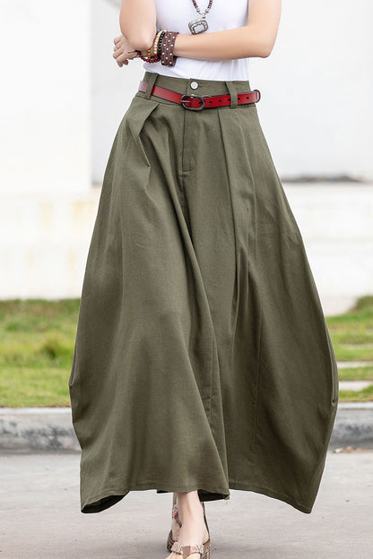 A woman wearing a green maxi skirt with a front zipper and buttons closure, featuring two side pockets and contrast patchwork details.