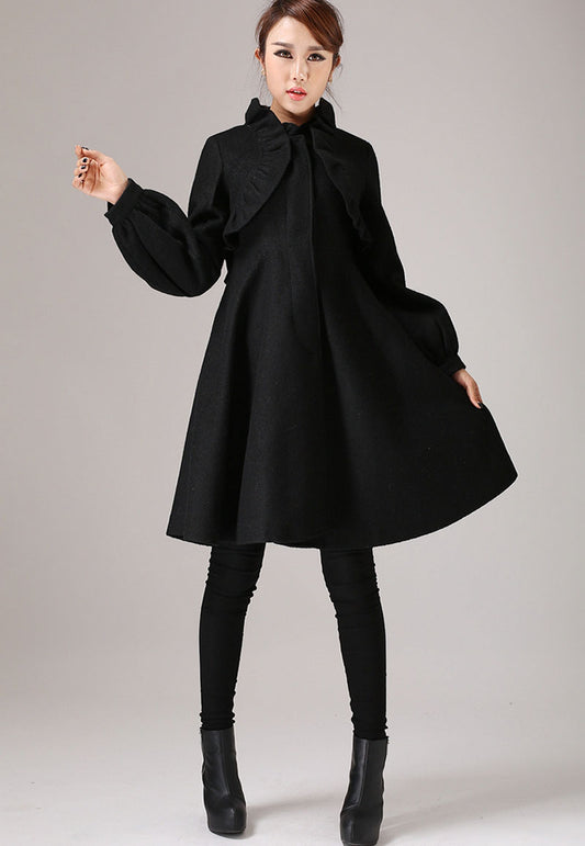 A woman modeling a black wool coat with ruffle detail, featuring a round neckline, long sleeves, and a front closure.