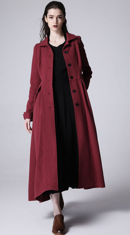 A woman standing and modeling a wine red linen long jacket with front buttons and long sleeves, paired with a black dress.